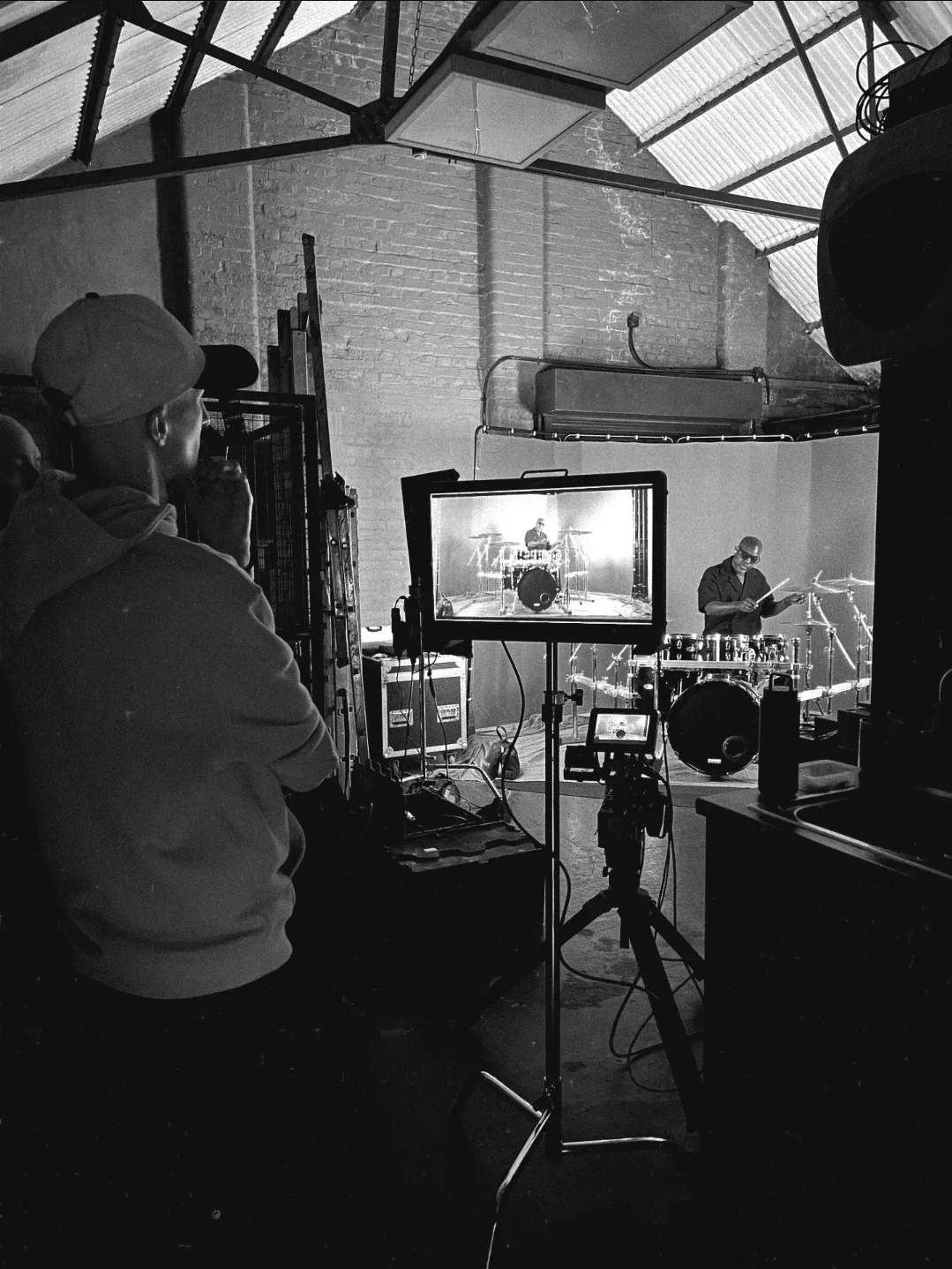 A crew member observing the production monitor as the drummer performs