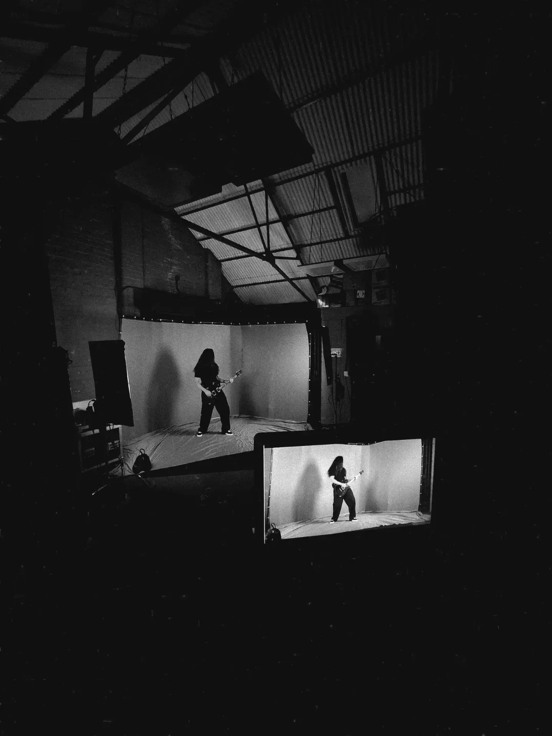Wide view down the studio as the guitarist performs against the curved backdrop, a live monitor in the foreground